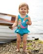 young girl stood next to a white rowing boat wearing the Frugi eco-friendly little mermaid swimming costume