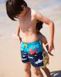 Young boy stood on some sand in the Frugi polkerris board swim shorts