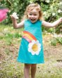 Young girl stood in a field holding a flower and wearing the Frugi organic cotton daisy penny shift dress