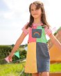 Girl stood in front of a tent wearing the Frugi eco-friendly zoey block colour rainbow dress