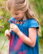 Close up of a young girl smelling a flower wearing the Frugi childrens floral gemma chambray dress