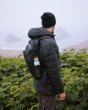 Man stood in front of some green bushes with the Klean Kanteen 20oz insulated classic metal bottle in the side pocket of his backpack