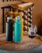 3 klean kanteen 750ml classic insulated bottles with the pour through cap on a wooden barrel next to some glasses of red wine