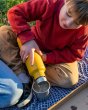 Close up of a young boy pouring liquid from a klean kanteen 750ml pour through bottle into a steel cup on a blue blanket