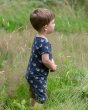 Young boy stood in a grass field wearing the Little Green Radicals organic cotton whale song shortie