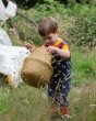 Child stood in some long grass holding a woven basket wearing the LGR eco-friendly whale song dungarees