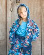 Girl stood wearing the Maxomorra organic cotton reversible zip hoodie and rib pants in the fairground print, in front of a wooden background