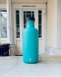 One Green Bottle 1200ml plastic free tough metal bottle on some white marble in front of a building door