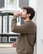 Man leaning against a wall drinking from the One Green Bottle life collection hunter camo canteen 