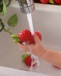 Close up of a childs hand holding the oli and carol soft rubber raspberry food toy under a running tap