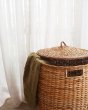 Close up of some green fabric hanging out of the Olli Ella eco-friendly tuscan lidded basket in front of a white curtain