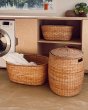 Olli Ella hand woven tuscan basket and lidded basket on a beige floor in front of some wooden cupboards
