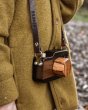 Close up of an O-WOW handmade dark oak wooden camera toy around the neck of a person wearing a brown woven coat
