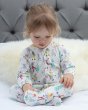 Girl sat on a white bed, looking down, wearing the Piccalily toddlers footed sleepsuit in the winter wonderland print