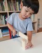 Boy playing with the plastic free Plan Toys woodwork saw on a white table in front of a large bookshelf