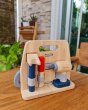 Plan Toys eco-friendly wooden carpenter role play tools set on a wooden table in front of a large window and green plant