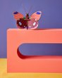 Studio roof eco-friendly delias butterfly slotting craft model balanced on a red sculpture block in front of a purple wall