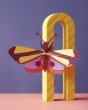 Studio roof slotting cardboard butterfly decoration climbing on a yellow arch in front of a purple background