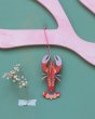 Studio Roof sustainable cardboard lobster ornament hanging from some pink wood in front of a green wall 