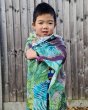 Young boy stood in front of a wooden fence with the large Wonder Cloths organic cotton jungle fabric wrapped around him