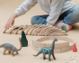 Close up of child playing with some dinosaur toys and a set of Abel mini wooden curved block toys on a beige background