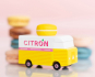 Picture of the Citron Candylab Candyvan. It is a 1960s style yellow and white van with a yellow Lemon Macaron on the roof. The background shows colourful macarons.