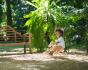 Toddler sat on the wooden foldable rocking horse by PlanToys. Side view outside in front of lush green foliage.