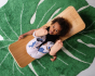 Child laying on a Wobbel Bamboo balance board on a green leaf carpet