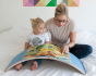 Woman and child reading a book on a Wobbel XL felted board on a bed