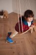 Young child leaning on the babai beige wooden rope swing in a wooden living room