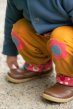 Small child wearing the Frugi reversible gold/scandi flower trousers with the ankles turned up with crouched knees