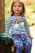 Girl sat on a green blanket wearing a stripy top and the Frugi eco-friendly rainbow flight snuggle bottoms 