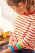 Close up of  a young girl holding an orange wearing the Frugi organic cotton long sleeved mylor striped top 