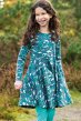 Smiling child wearing the Frugi Long sleeve organic cotton teal skater dress with cosmic wave print of narwhals, whales and galaxy inspired star prints with teal tights with trees in the background