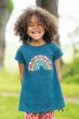Girl wearing emery short sleeve a-line rainbow printed top by frugi outside smiling