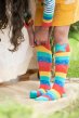 Girl pulling up Frugi knee high Hygge rainbow stripe socks with turquoise star on knee  wearing yellow dress and striped rainbow sleeve top