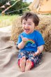 Boy sat on some beige fabric leaning on a hay bail wearing the Frugi rainbow skies soft trousers