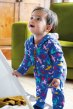 Baby wearing Frugi eco friendly rainbow flight snuggle suit with green sofa behind him, holding edge of a tipi tent