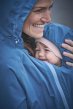Mamalila Shelter Babywearing Rain Jacket in Vintage Blue. Lifestyle view of this technical babywearing rain coat with parent and baby, hood up