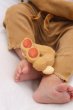 Close up of the oli and carol childrens rubber peanut food toy on a toddlers legs on a white background