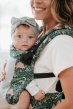 Close up of a small baby in a Tula free to grow adjustable soft baby carrier in a white room 