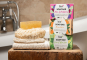 Bio-d natural plum and mulberry solid soap bar, mandarin soap bar, lime and aloe vera soap bar on a wooden block with wash cloths and sponge next to the soap boxes