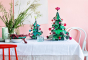Studio Roof Large cardboard Christmas Tree & smaller cardboard Christmas tree on a table in front of a pink wall