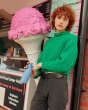 An adult stood next to a pink ice cream cone and wearing a bright green jumper is holding their One Green Bottle 350ml Evolution Collection Bottle - Sports Cap in Ocean