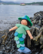 Close up of the Ambrosius eco-friendly blue felt mermaid toy in some seaweed in front of the ocean  