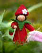 Close up of an Ambrosius handmade felt strawberry fairy figure stood on some grass next to a pink flower