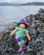 Close up of the Ambrosius purple mermaid collectable felt doll in some seaweed in front of the sea