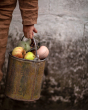 Close up of a childs hand carrying a metal bucket full of apples and a Babai wooden apple toy 