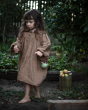 Young girl wearing a brown outfit walking away from a metal bucket full of fruit holding a Babai wooden pear toy