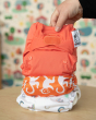 Close up of a hand holding a Close Pop-in reusable baby nappy over a stack of reusable one size nappies